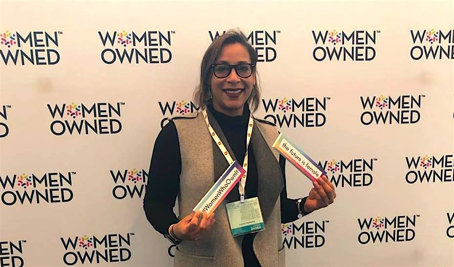 Woman smiling in front of banner saying "women owned".
