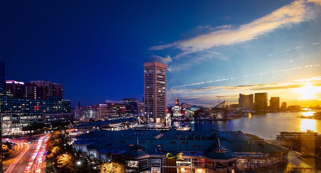 View of Baltimore's Inner Harbor during sunset with World Trade Center, Aquarium, and downtown buildings visible.