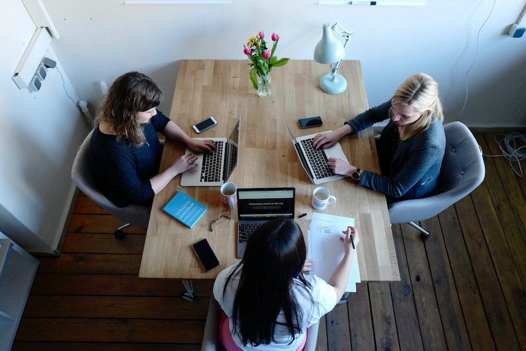 Three women sitting at a table with laptop computers and cell phones, photo taken from above