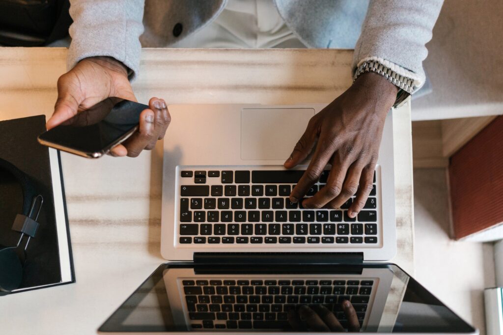 Hands typing on computer and holding a cell phone