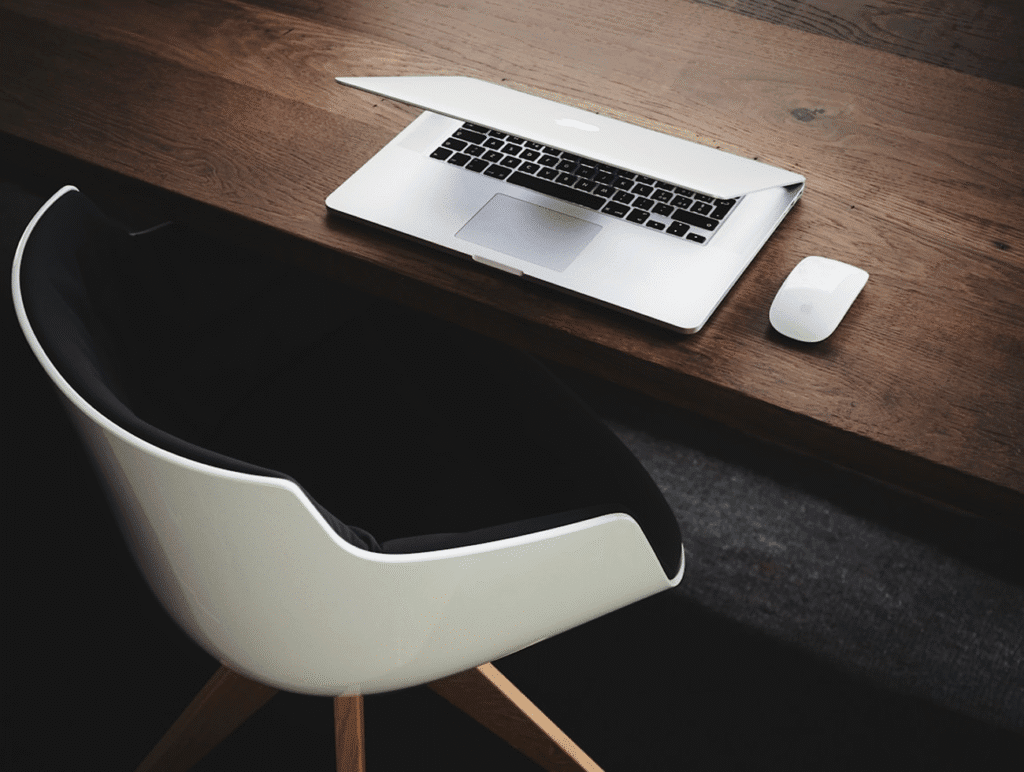 Minimalist workspace with a partially closed laptop, mouse, and modern chair on a wooden desk.