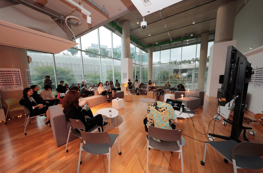 Indoor creative workshop with participants seated, attentive to a speaker in a modern, open space with large windows.