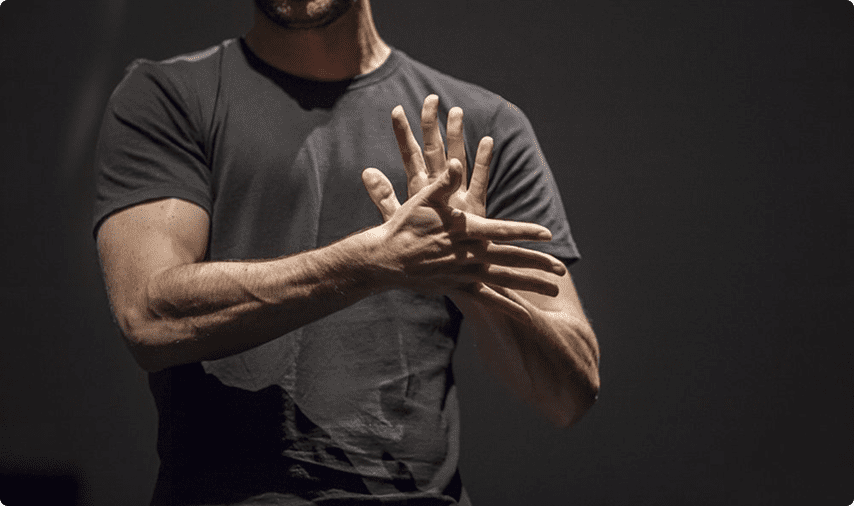 Person in dark shirt using expressive hand gestures against a dark background.