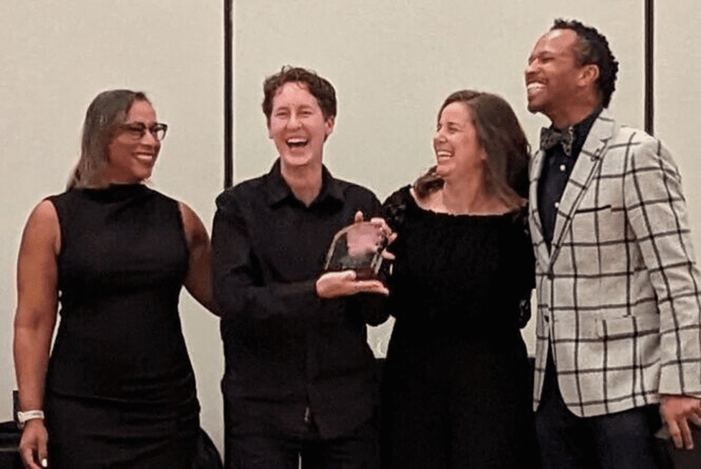 Four people happily present an award together at an event, wearing formal attire.