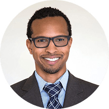 Smiling professional man in suit and glasses, headshot on plain background.