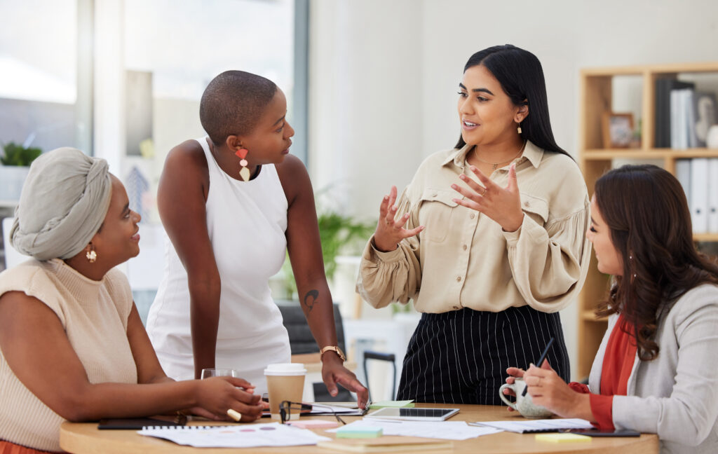 Team collaboration in an office setting with four diverse women discussing ideas.