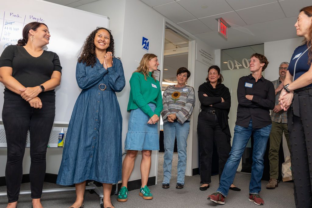 Group of people smiling and standing in a circle during a casual office meeting.