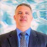 Man in suit with a water-like background, looking ahead confidently.